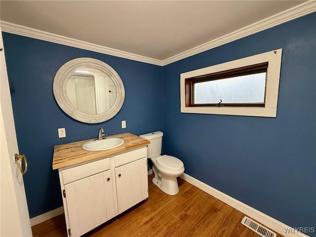 half bath with vanity, toilet, baseboards, wood finished floors, and visible vents