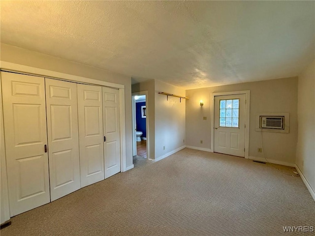 foyer entrance featuring light colored carpet, baseboards, a wall mounted AC, and a textured ceiling
