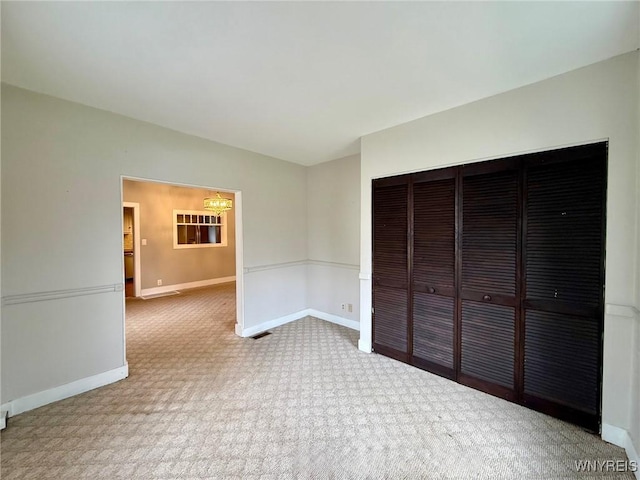 unfurnished bedroom featuring carpet flooring, a notable chandelier, baseboards, visible vents, and a closet