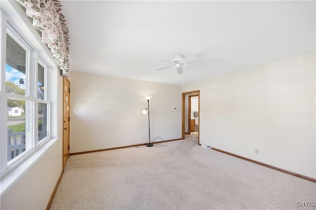 unfurnished room featuring baseboards, a ceiling fan, light colored carpet, and a wealth of natural light