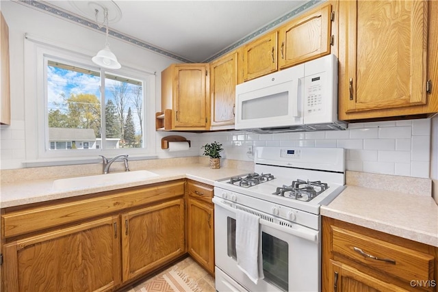 kitchen with a sink, light countertops, pendant lighting, and white appliances