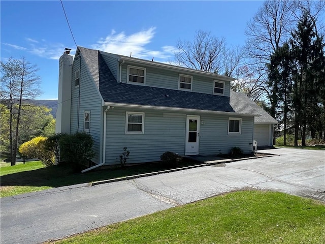 exterior space with driveway, a chimney, a garage, a front lawn, and a shingled roof