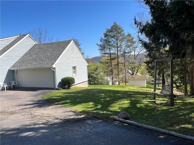 view of home's exterior with a garage, a shingled roof, a lawn, and driveway