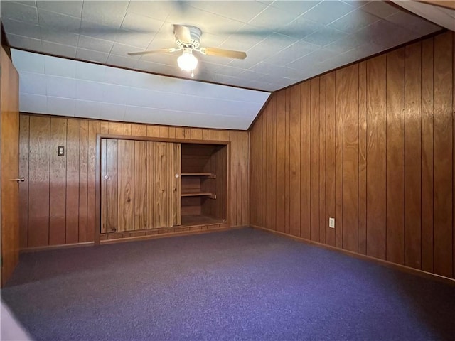 interior space with carpet floors, ceiling fan, wood walls, and baseboards