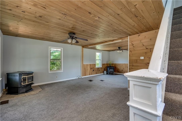 11931 State Route 12e, Lyme, NY 13622 - unfurnished living room featuring a wood stove, wood walls, ceiling fan, carpet flooring, and a wainscoted wall