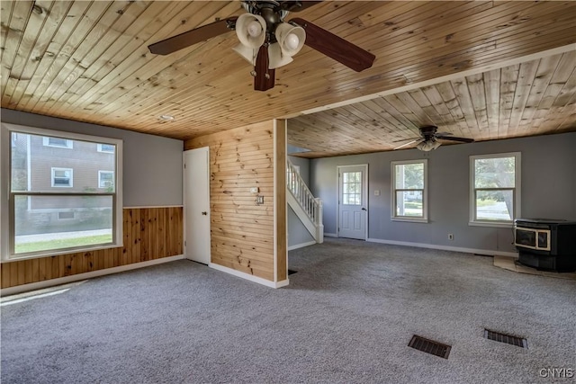 11931 State Route 12e, Lyme, NY 13622 - unfurnished living room with wooden walls, ceiling fan, a wood stove, stairs, and carpet flooring