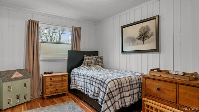 bedroom featuring crown molding, wood walls, and wood finished floors