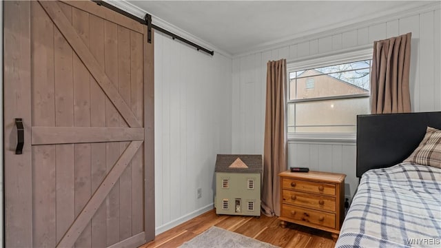 bedroom with baseboards, a barn door, wood finished floors, and ornamental molding