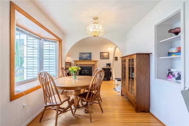 dining room featuring arched walkways, baseboards, light wood-style flooring, and a notable chandelier