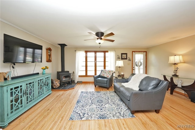 living area with crown molding, a ceiling fan, wood finished floors, and a wood stove