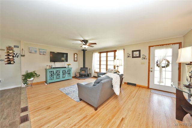 living area featuring crown molding, a wood stove, wood finished floors, baseboards, and ceiling fan