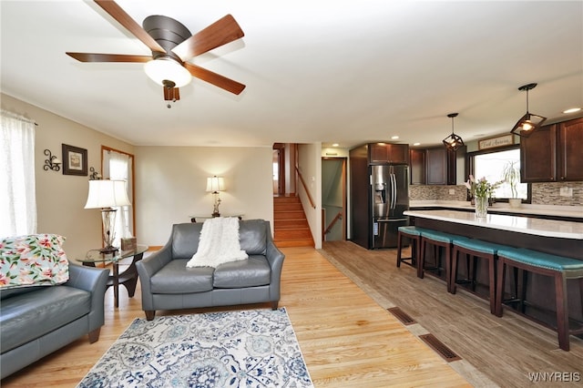 living area with ceiling fan, recessed lighting, light wood-type flooring, visible vents, and stairway