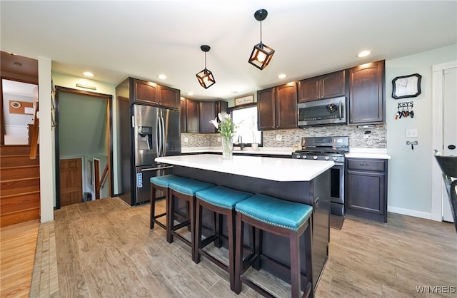 kitchen featuring dark brown cabinets, light wood-type flooring, light countertops, tasteful backsplash, and appliances with stainless steel finishes
