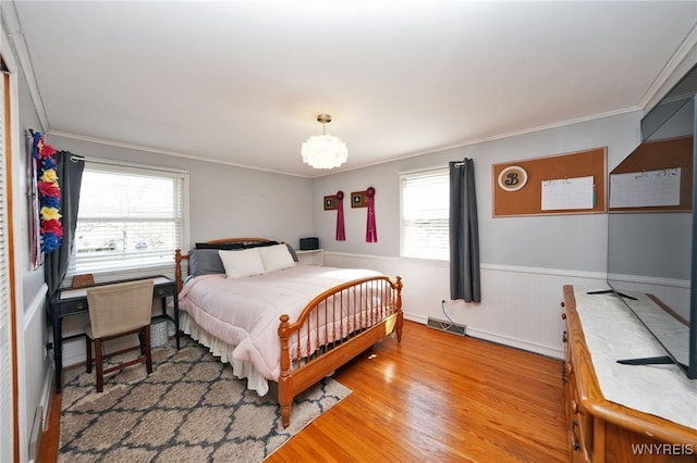 bedroom featuring a wainscoted wall, ornamental molding, multiple windows, and visible vents