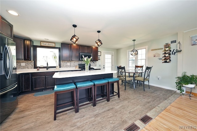 kitchen with freestanding refrigerator, decorative backsplash, a kitchen breakfast bar, light countertops, and stainless steel microwave