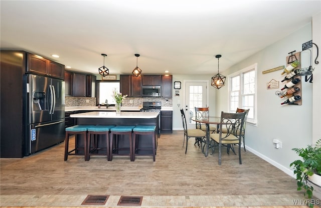 kitchen with appliances with stainless steel finishes, tasteful backsplash, a center island, dark brown cabinets, and light countertops