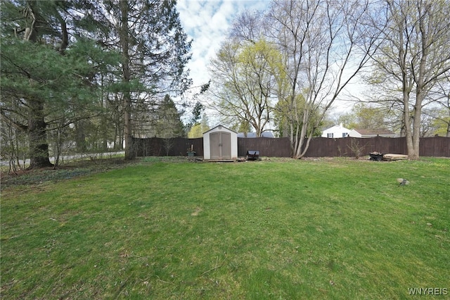 view of yard with a fenced backyard, a storage unit, and an outbuilding