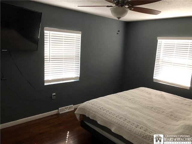 bedroom featuring visible vents, a ceiling fan, baseboards, and dark wood-type flooring