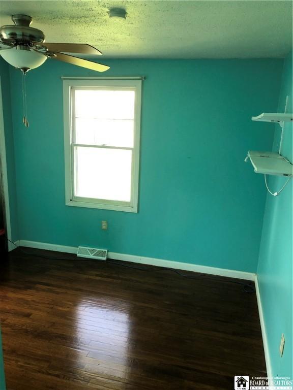 spare room featuring dark wood-style flooring, baseboards, visible vents, and a ceiling fan