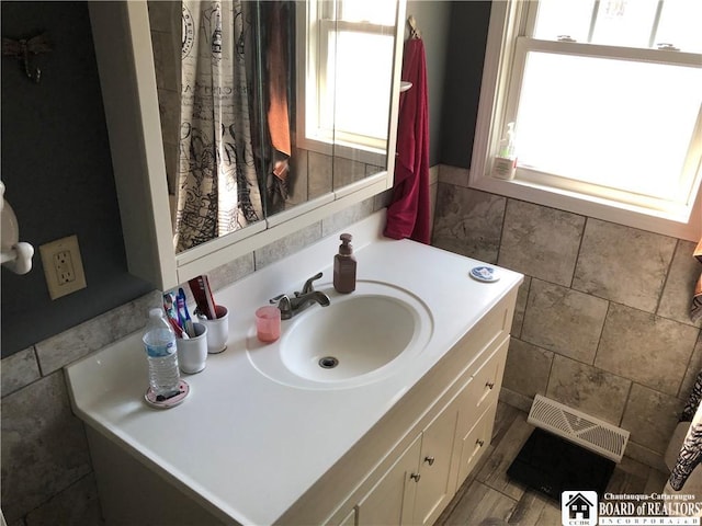 bathroom featuring plenty of natural light, vanity, visible vents, and tile walls