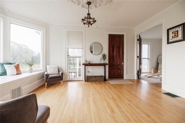 sitting room with a healthy amount of sunlight, wood-type flooring, a notable chandelier, and visible vents
