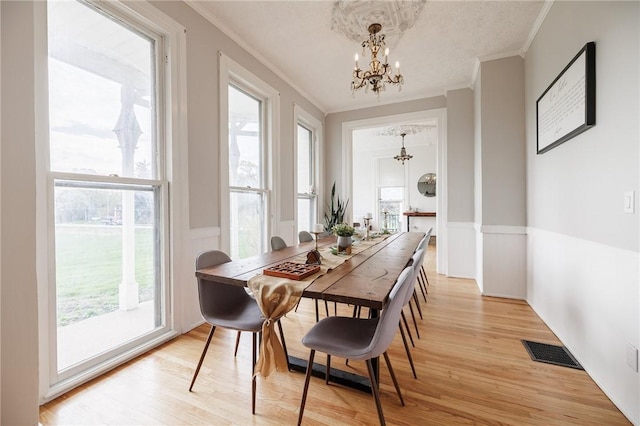 dining room featuring crown molding, visible vents, an inviting chandelier, and a wainscoted wall