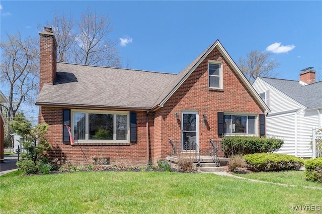 tudor-style house featuring roof with shingles, a chimney, a front lawn, and brick siding