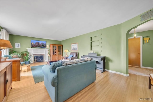living area featuring a fireplace, arched walkways, baseboards, and light wood-type flooring