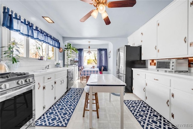 kitchen with appliances with stainless steel finishes, arched walkways, a ceiling fan, white cabinetry, and a toaster