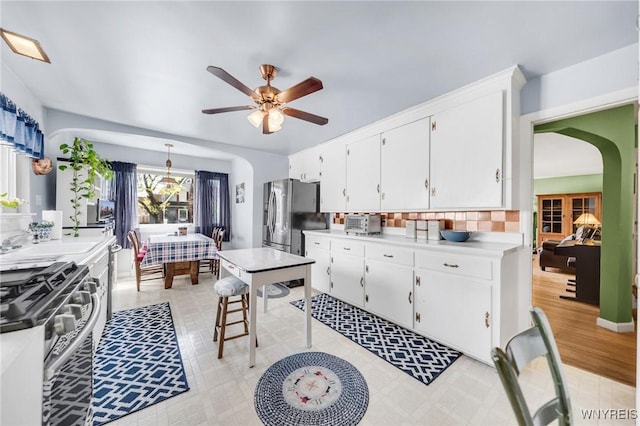 kitchen with ceiling fan, light countertops, white cabinetry, arched walkways, and stainless steel appliances
