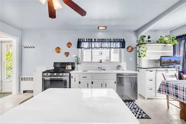 kitchen featuring ceiling fan, appliances with stainless steel finishes, a sink, radiator heating unit, and white cabinetry
