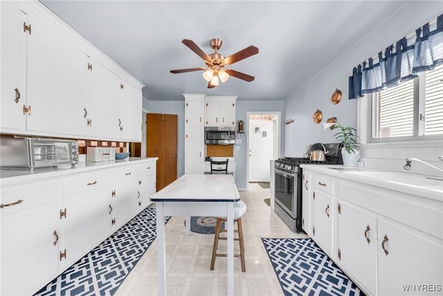 kitchen with a ceiling fan, a toaster, light countertops, stainless steel appliances, and white cabinetry