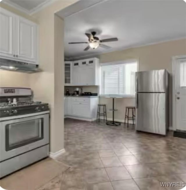 kitchen with appliances with stainless steel finishes, white cabinetry, a ceiling fan, under cabinet range hood, and ornamental molding