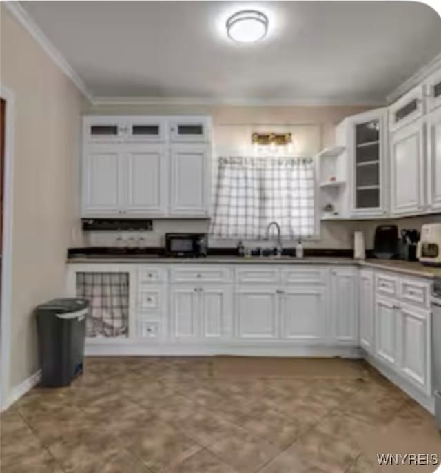 kitchen with crown molding, dark countertops, glass insert cabinets, white cabinets, and a sink