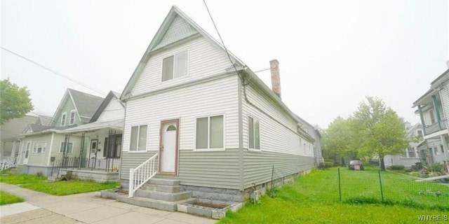 view of front of property featuring covered porch, a chimney, and a front lawn