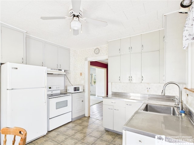 kitchen with a sink, stainless steel countertops, white appliances, a ceiling fan, and under cabinet range hood
