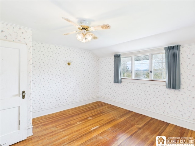 empty room with a ceiling fan, baseboards, wallpapered walls, wood finished floors, and vaulted ceiling