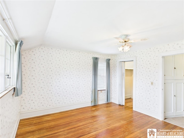 unfurnished bedroom with light wood-type flooring, lofted ceiling, multiple windows, and wallpapered walls