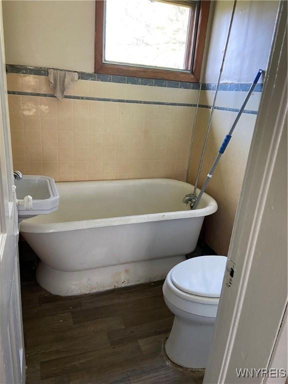 bathroom featuring a freestanding tub, wood finished floors, toilet, and tile walls