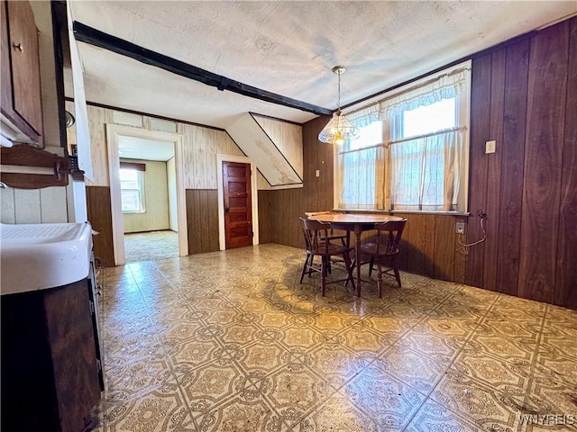 dining area with a textured ceiling, beamed ceiling, and wood walls