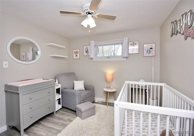 bedroom featuring wood finished floors, baseboards, ceiling fan, and a nursery area