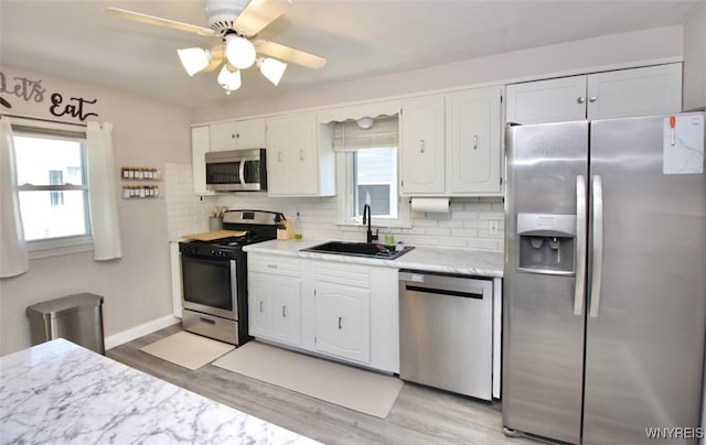 kitchen with white cabinets, a sink, light countertops, stainless steel appliances, and backsplash