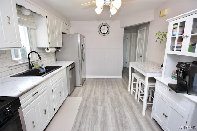kitchen with stainless steel dishwasher, a sink, white cabinetry, and black stove