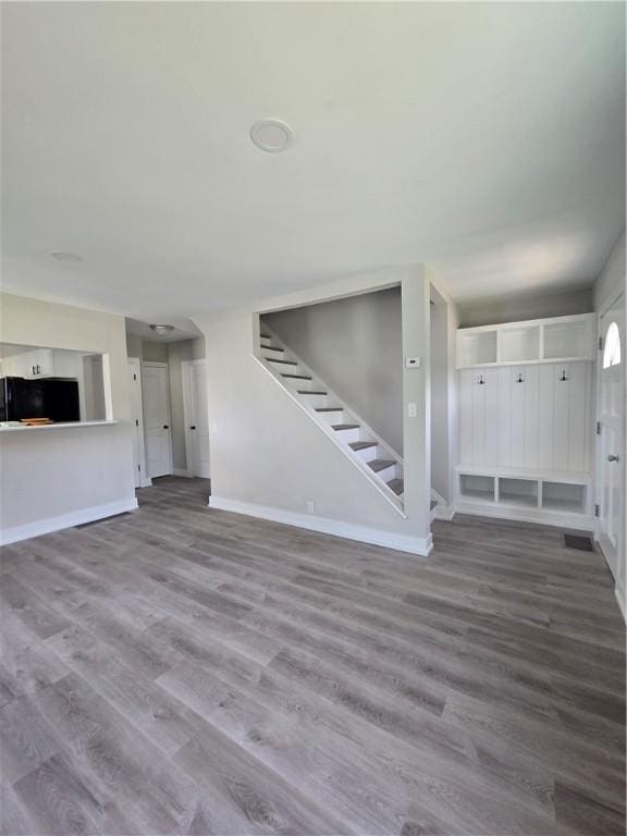 unfurnished living room with stairway, baseboards, and wood finished floors