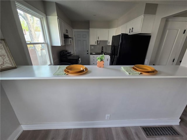 kitchen with visible vents, freestanding refrigerator, dark wood-type flooring, under cabinet range hood, and a sink