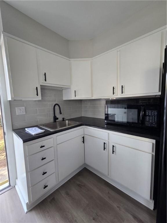 kitchen with black microwave, dark countertops, decorative backsplash, and a sink
