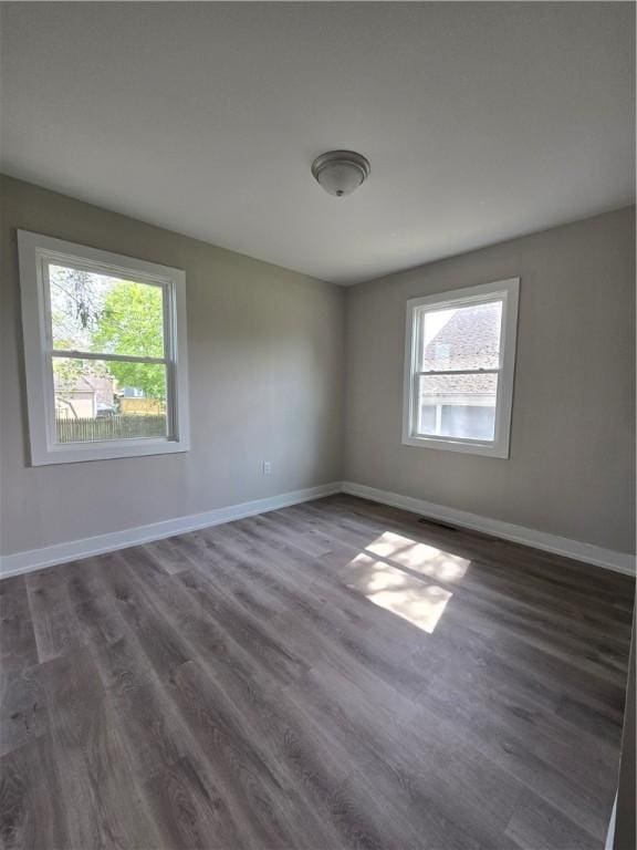 spare room with baseboards, visible vents, dark wood-style flooring, and a wealth of natural light