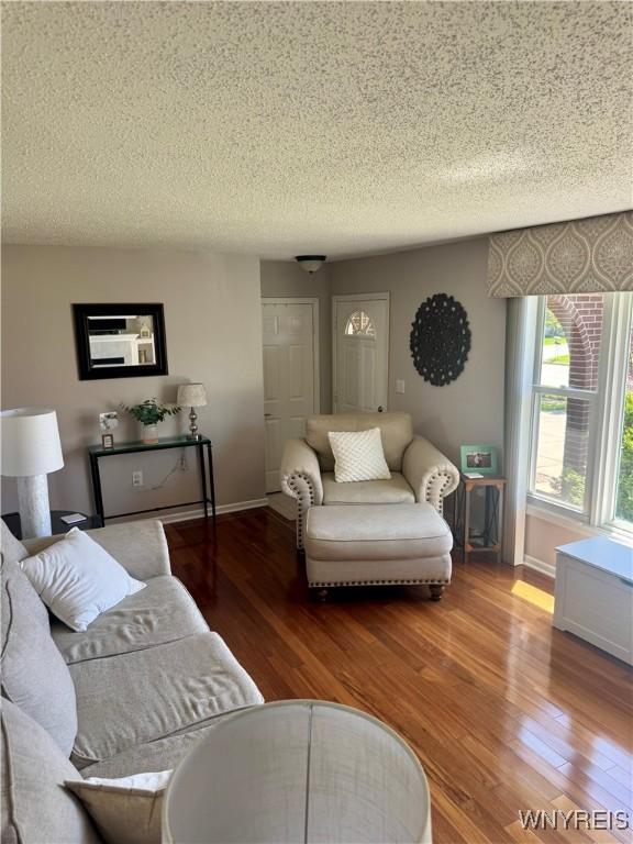 living area with baseboards, a textured ceiling, and wood finished floors