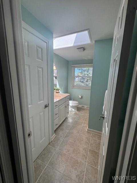 bathroom featuring vanity, toilet, baseboards, a skylight, and visible vents