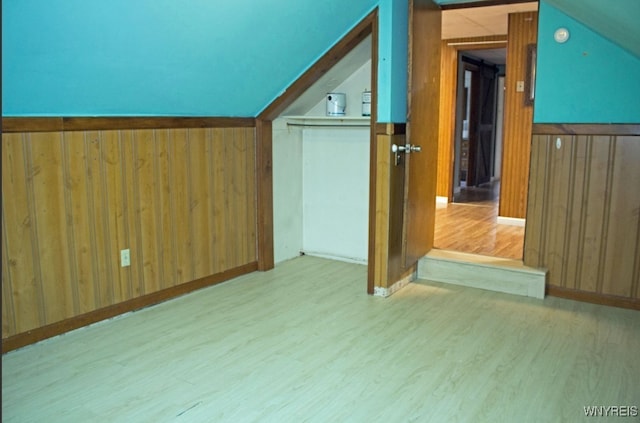 additional living space with vaulted ceiling, wood walls, and wood finished floors